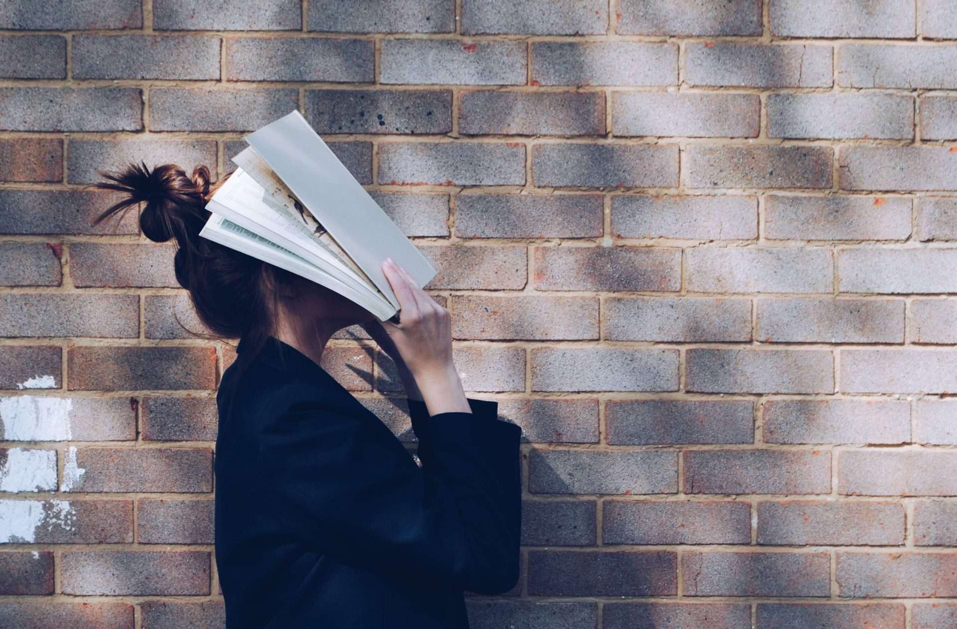 Junge Frau, die ein Buch vor ihr Gesicht schlägt
